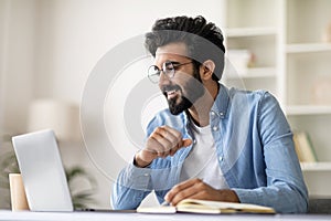 Indian man using laptop and taking notes while working at home office