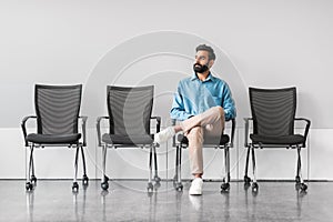 Indian man waiting calmly in office with empty chairs