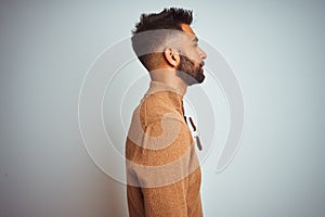 Indian man wearing elegant sweater and sunglasses standing over isolated white background looking to side, relax profile pose with