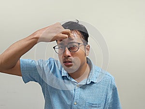 Indian man wearing glasses and a blue shirt showing headache against a gray background