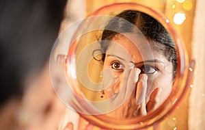 Indian married Woman applying Bindi, sindoor or decorative mark to forehead in front of mirror during festival photo