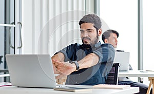 Indian millennial tired exhausted sleepy bearded dull face male businessman sitting at workstation desk with laptop computer