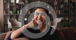 Indian millennial woman sit on sofa smile look at camera