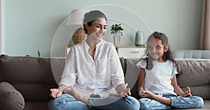 Indian mom and little daughter meditating seated on couch