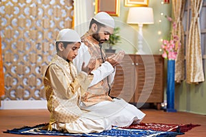 Indian Muslim father with kid doing namaz or praying during ramadan festival celebration at home - concept of ramzan