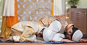 Indian Muslim father with kid doing namaz or praying during ramadan festival celebration at home - concept of ramzan