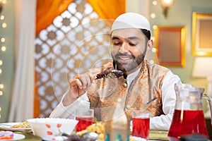 Indian Muslim young man enjoys eating chicken leg piece during during ramadan iftar dining at home - concept of healthy