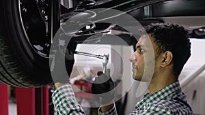 Indian or pakistani auto mechanic working under car on hydraulic lift in garage