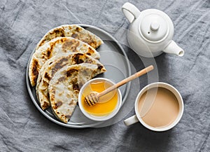 Indian paratha flatbread with honey and masala tea on grey background, top view