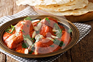 Indian popular food Butter Chicken Murgh Makhani with spicy sauce, almonds and cilantro close-up on a plate with roti on