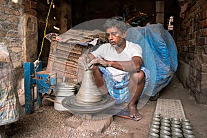 Indian potter making small pot or Diya for Diwali with clay on potters wheel in his small factory. Manufacturing traditional