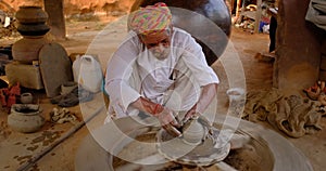 Indian potter at work throwing the potter's wheel and shaping clay ware: pot, jar in pottery workshop. Rajasthan