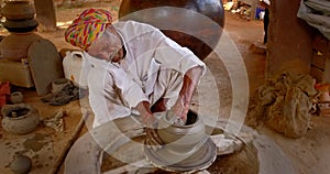 Indian potter at work throwing the potter's wheel and shaping clay ware: pot, jar in pottery workshop. Rajasthan