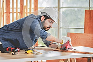 Indian professional bearded male engineer architect foreman labor worker carpenter wears safety helmet and gloves using wood