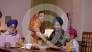 Indian Punjabi lady in ethnic wear serving food to her family with love - Army man with his father, son, and wife