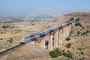 Indian railways long passenger train, exiting a tunnel to cross a tall railway bridge