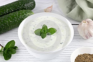 Indian raita sauce with dahi yogurt, cucumber and herbs. Greek tzatziki sauce on a white wooden background.