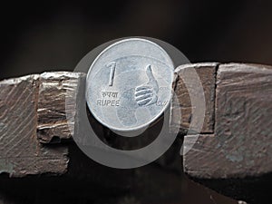 Indian rupee coin clamped in a metal vise on both sides.