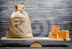 Indian rupee INR symbol money bag and a bunch of boxes on scales. Trade exchange balance. Import and export, economic processes.