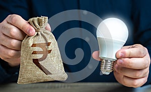Indian rupee money bag and burning idea light bulb in the hands of a man.