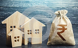 Indian rupee money bag and figurines of residential buildings. Property tax. Municipal budgeting. Financing urban development