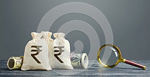 Indian rupee money bags and magnifying glass. Profitable investment, dividends payouts. Financial monitoring of suspicious cash photo