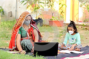 Indian rural mother teaching daughter online on laptop using internet.
