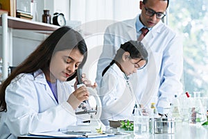 Indian scientist woman student using microscope do an experiment at biology class in school laboratory while teacher teaching