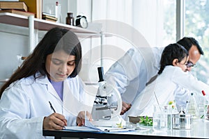 Indian scientist woman student using microscope do experiment and record results of experiment at biology class in school