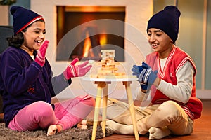 Indian siblings kids in winter wear playing wooden blocks building game at home during winter holidays at home - concept