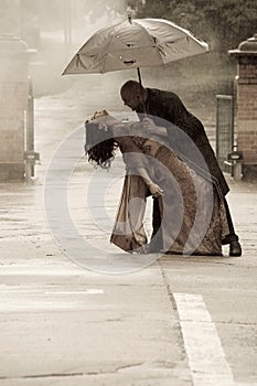 Indian smartly dressed couple dancing under an umbrella in the rain.