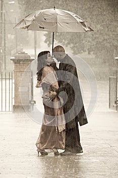 Indian smartly dressed couple holding an umbrella in the rain.