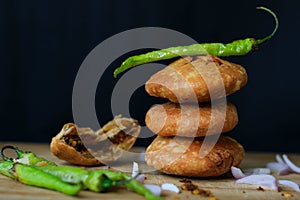 Indian snack kachori served with green chilli and onions in a black background