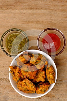 Indian snack pakora with tomato sauce or chutney on wooden background with copy space