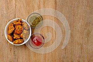 Indian snack pakora with tomato sauce or chutney on wooden background with copy space