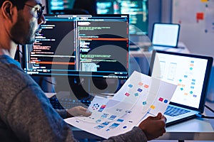 Indian software development working on coding computer screen and flowchart at night in modern office