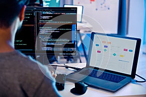 Indian software development working on coding computer screen and flowchart at night in modern office