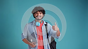 indian or spanish male student with backpack and laptop showing thumbs up gesture of approval while standing against