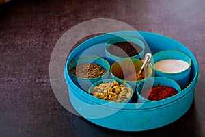 Indian spice box on wooden background with copy space,Cardamom, turmeric, chilli powder, salt,mustard seeds,cumin, selective focus
