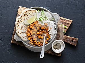 Indian spicy chickpeas curry with rice and naan bread in pan on dark background, top view photo