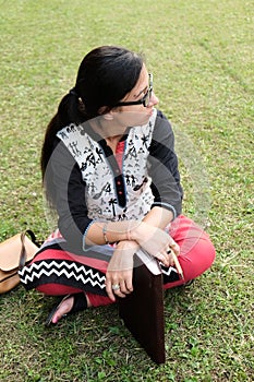 Indian student sitting in a college lawn and thinking with a pen and book