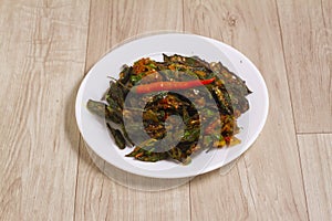 Indian style Masala Sabji OR Sabzi of fried Bhindi OR Okra also known as Ladyfinger, Served in a bowl over wooden background.