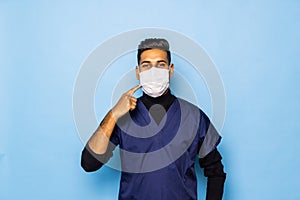 A indian surgeon standing setting his gloves to start the surgery, wearing a mask and a blue uniform on a blue background