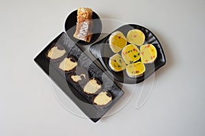 Indian sweet food mithai. Milk cake, chocolate rolls, and pineapple rolls with black dishes and black background. Milk products.