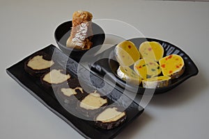 Indian sweet food mithai. Milk cake, chocolate rolls, and pineapple rolls with black dishes and black background. Milk products.