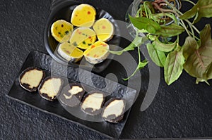 Indian sweet food mithai. Milk cake, chocolate rolls, and pineapple rolls with black dishes and black background. Milk products.