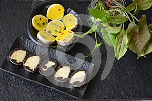 Indian sweet food mithai. Milk cake, chocolate rolls, and pineapple rolls with black dishes and black background. Milk products.