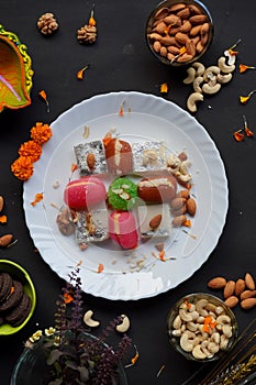 Indian sweets in a plate including cutlus, sandwich, barfi, petha garnished with almond, pistachio, cashews