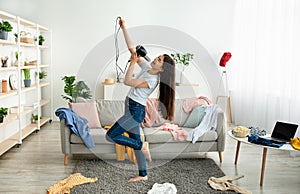 Indian teenage girl dancing and singing in messy room, using blowdryer as microphone, giving domestic concert