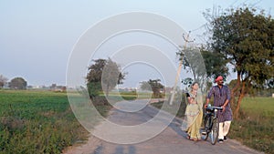An Indian village couple going for a walk on a village road with a bicycle - a village scene